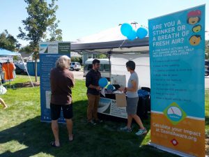 Booth at festival with balloons, banners about the NFRMPO and air quality, and three people